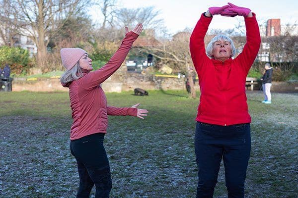 One adult woman showing an older woman how to stretch in a park